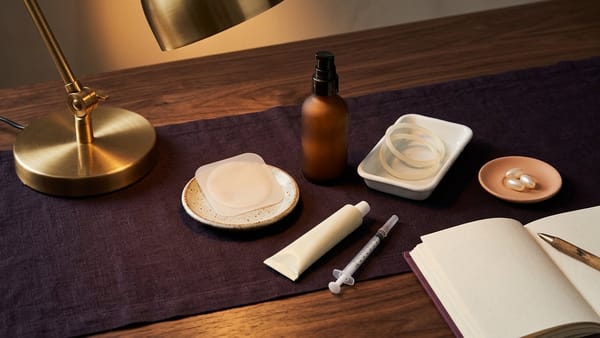 3D studio still-life of a transdermal hormone patch, amber gel pump, vaginal ring, cream tube with dosing syringe, and softgel capsules.