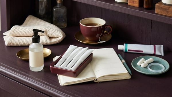 Dark plum shelf with lubricant pump, vaginal moisturiser applicators, estrogen cream, pessaries, blank notebook, towel and cup of tea.